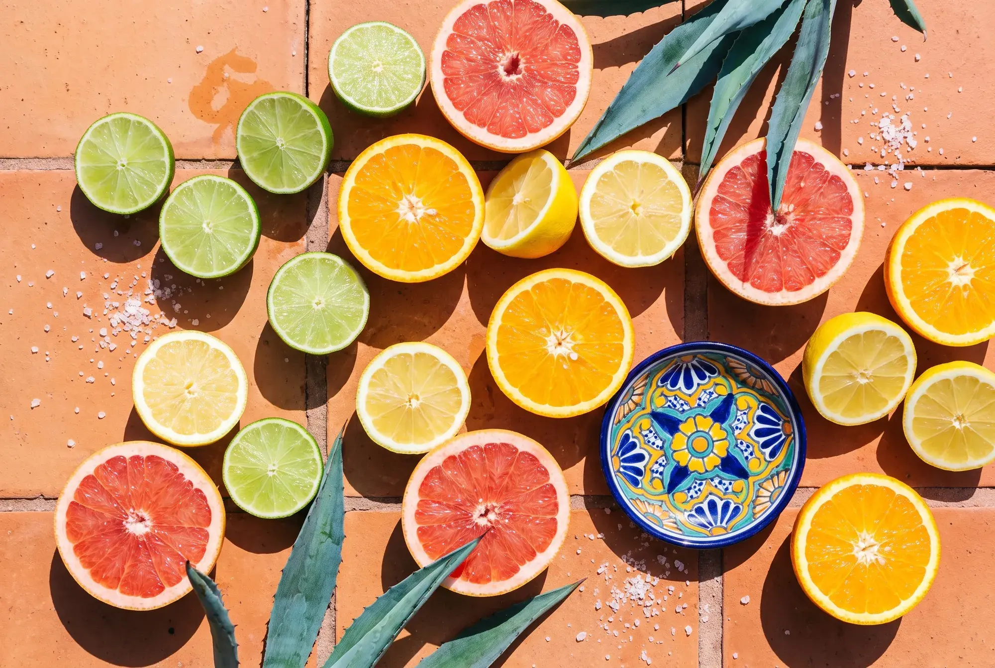 Overhead flat lay of halved limes, lemons, oranges and grapefruit on a cream stone surface