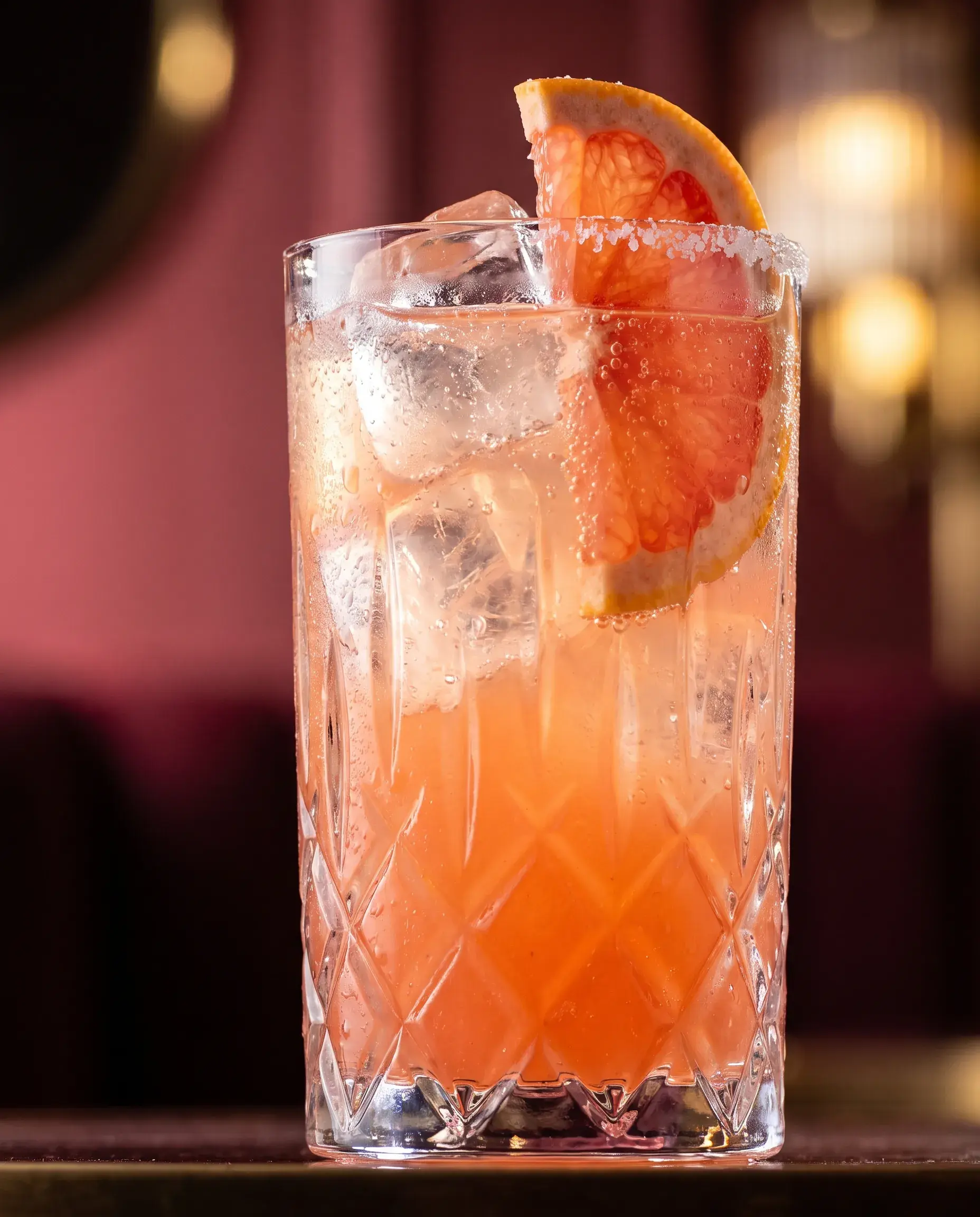 A paloma in a tall highball with grapefruit wedge, backlit so the drink glows